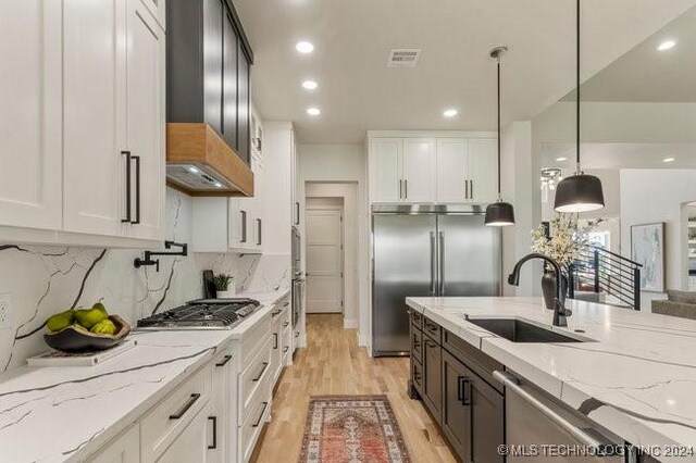 kitchen with hanging light fixtures, stainless steel appliances, sink, premium range hood, and white cabinetry