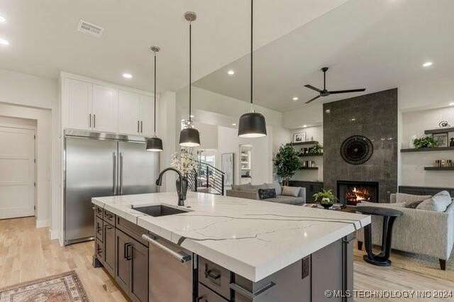 kitchen with appliances with stainless steel finishes, sink, a fireplace, pendant lighting, and white cabinets