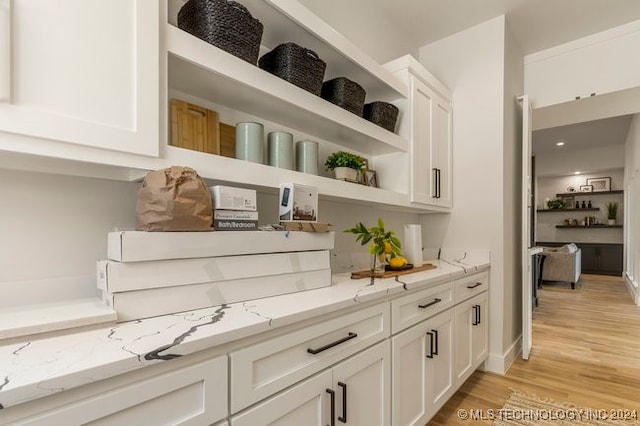 bar featuring light stone countertops, light hardwood / wood-style flooring, and white cabinetry