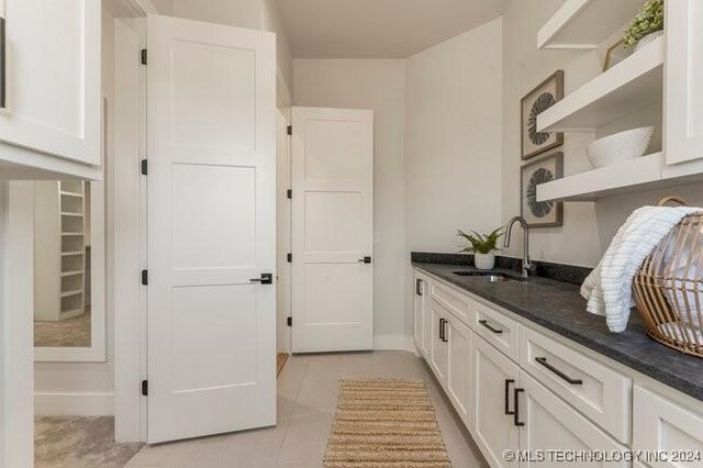 interior space featuring white cabinetry, light tile patterned floors, dark stone countertops, and sink