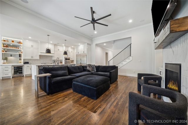 living room featuring ornamental molding, wine cooler, a large fireplace, and dark wood-type flooring