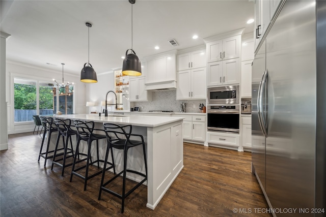 kitchen featuring built in appliances, pendant lighting, white cabinetry, and an island with sink