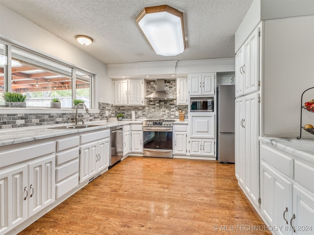 kitchen with appliances with stainless steel finishes, light hardwood / wood-style floors, wall chimney exhaust hood, and sink