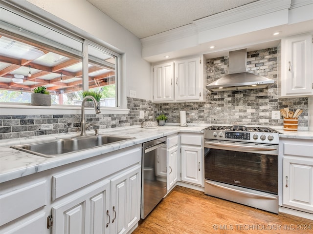 kitchen featuring white cabinets, stainless steel appliances, tasteful backsplash, and wall chimney range hood