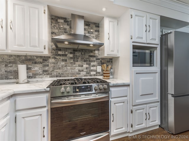 kitchen featuring backsplash, wall chimney exhaust hood, appliances with stainless steel finishes, light stone counters, and white cabinetry