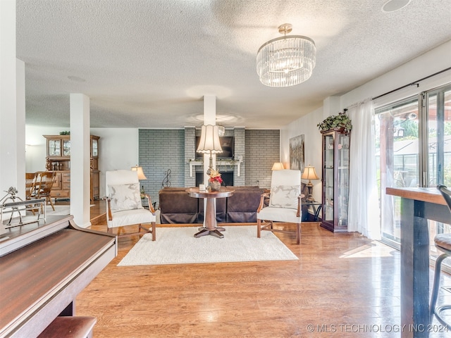 living room featuring a brick fireplace, a chandelier, a textured ceiling, and hardwood / wood-style flooring