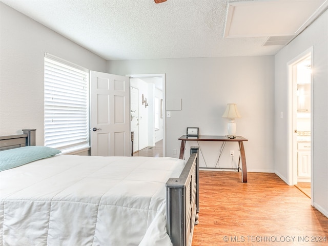 bedroom with a textured ceiling, ensuite bathroom, and light hardwood / wood-style flooring