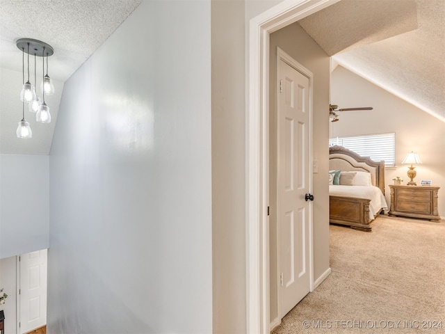 hallway featuring light colored carpet, lofted ceiling, and a textured ceiling