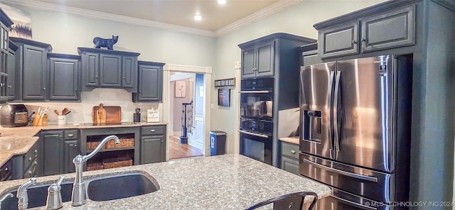 kitchen with sink, double oven, light stone counters, stainless steel fridge, and crown molding