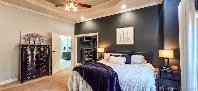 bedroom featuring ceiling fan, connected bathroom, a tray ceiling, ornamental molding, and light colored carpet