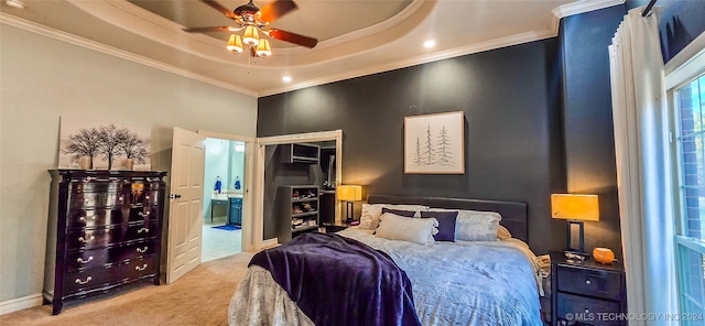 bedroom featuring ceiling fan, a tray ceiling, ornamental molding, ensuite bathroom, and light colored carpet