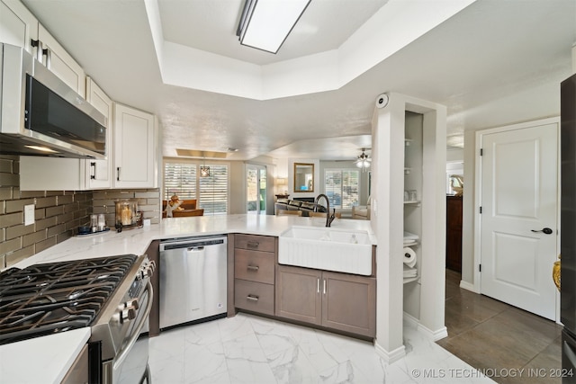 kitchen featuring appliances with stainless steel finishes, sink, backsplash, kitchen peninsula, and white cabinetry