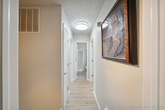 hallway with light hardwood / wood-style flooring and a textured ceiling