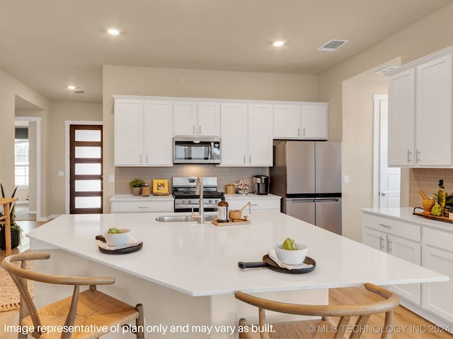 kitchen featuring tasteful backsplash, a center island with sink, white cabinets, and stainless steel appliances