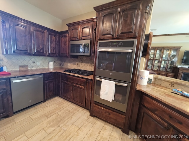 kitchen with appliances with stainless steel finishes, dark brown cabinetry, tasteful backsplash, and light hardwood / wood-style floors