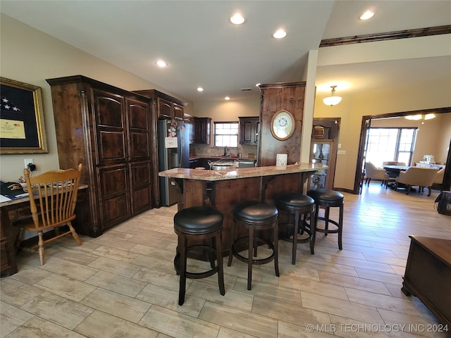 kitchen with tasteful backsplash, light stone countertops, a kitchen bar, dark brown cabinetry, and stainless steel fridge with ice dispenser