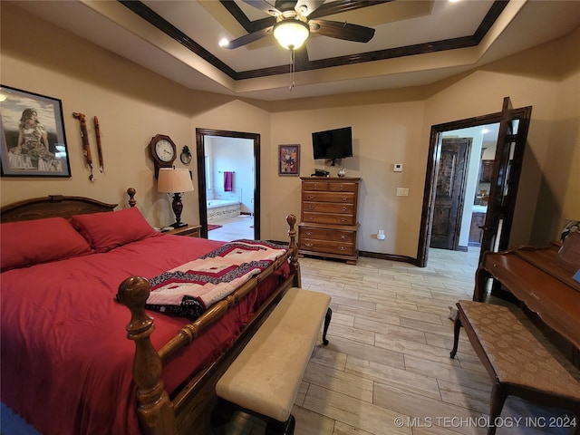 bedroom with connected bathroom, ornamental molding, a tray ceiling, and light wood-type flooring