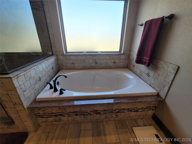 bathroom with a relaxing tiled tub and hardwood / wood-style flooring