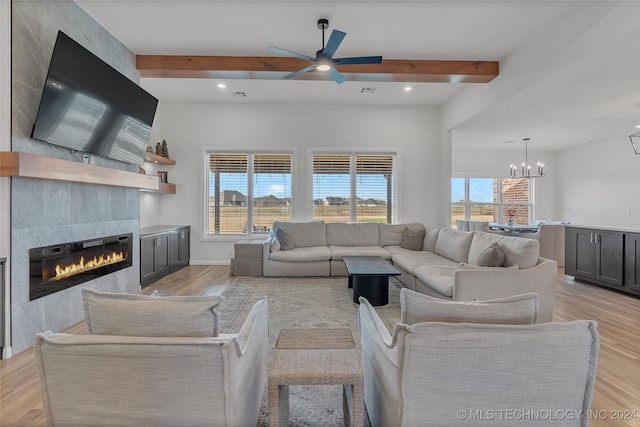 living room featuring beam ceiling, a premium fireplace, light hardwood / wood-style floors, and ceiling fan with notable chandelier