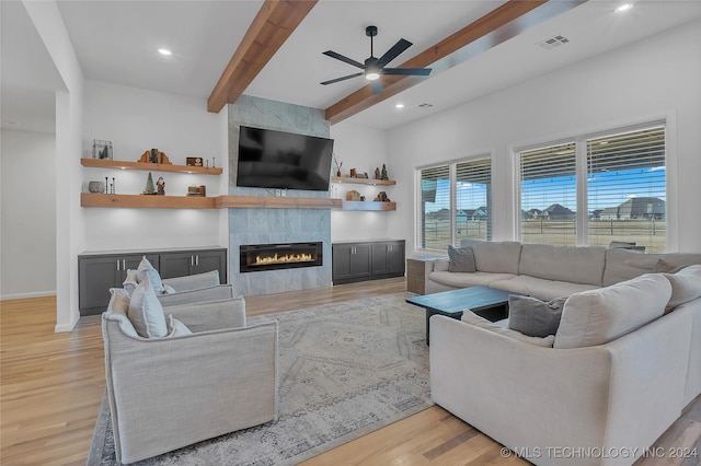 living room with beamed ceiling, light hardwood / wood-style floors, ceiling fan, and a tiled fireplace