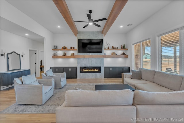 living room with beam ceiling, a tile fireplace, ceiling fan, and light wood-type flooring