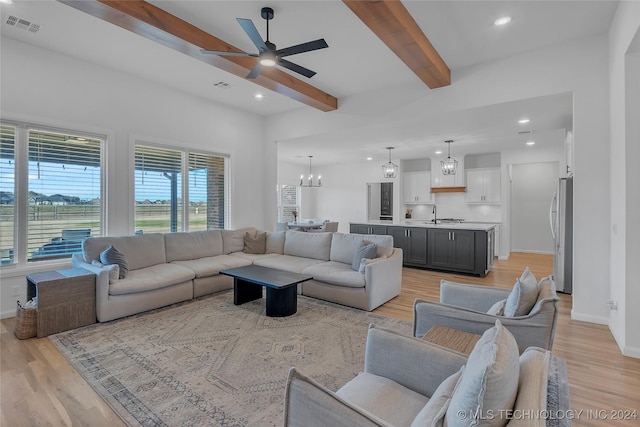 living room with beamed ceiling, ceiling fan with notable chandelier, light hardwood / wood-style floors, and sink