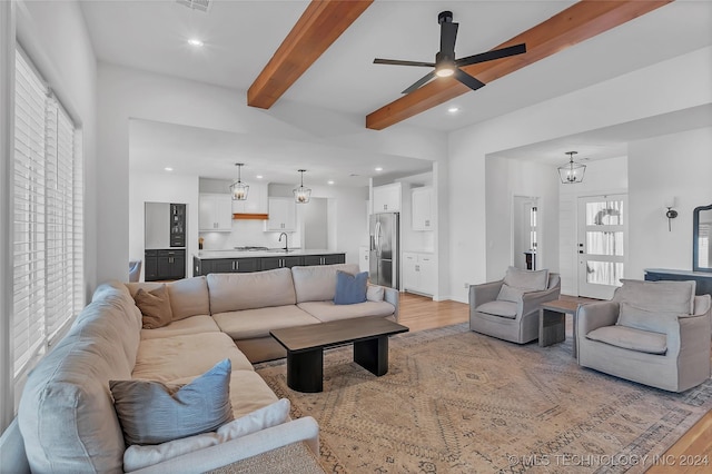 living room with beam ceiling, light hardwood / wood-style flooring, ceiling fan with notable chandelier, and sink