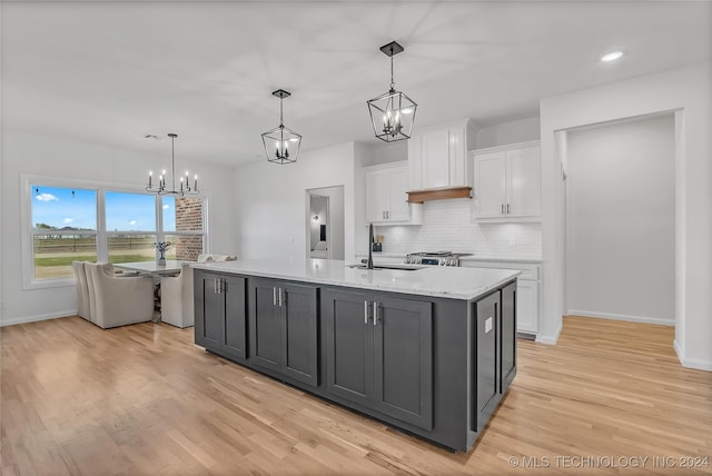 kitchen with sink, hanging light fixtures, light hardwood / wood-style floors, a center island with sink, and white cabinets