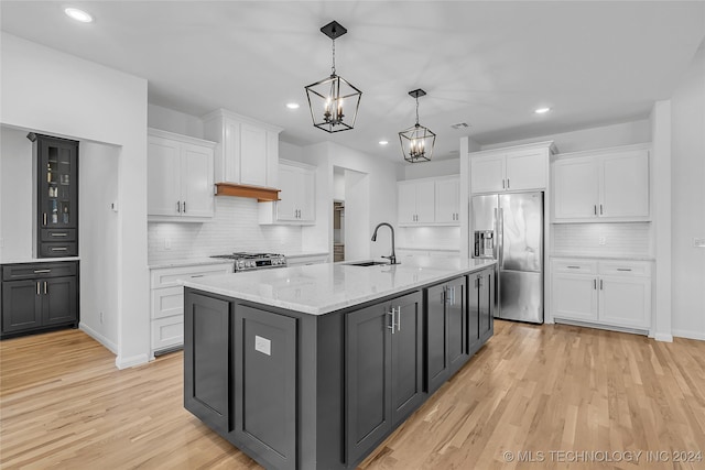 kitchen featuring stainless steel appliances, decorative light fixtures, light hardwood / wood-style flooring, white cabinetry, and an island with sink