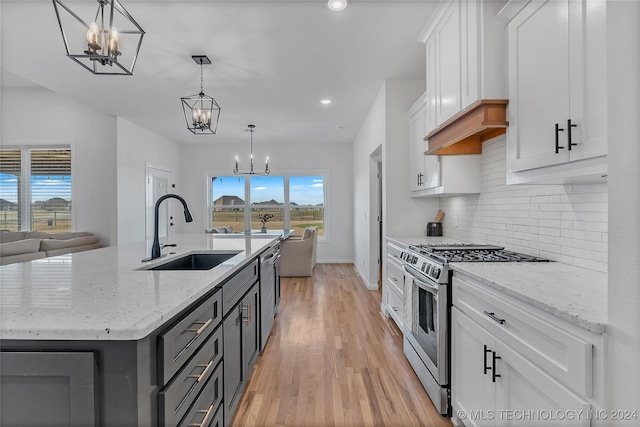 kitchen with a kitchen island with sink, sink, stainless steel stove, decorative light fixtures, and white cabinetry