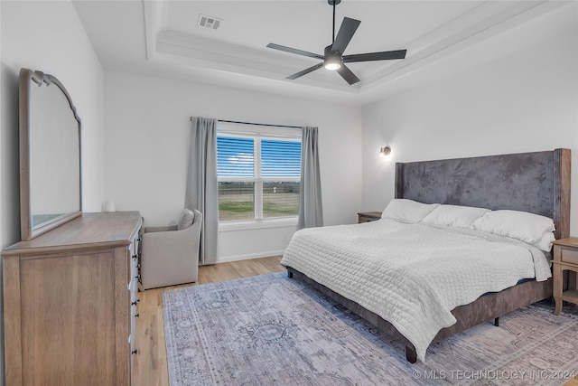 bedroom featuring light wood-type flooring, a tray ceiling, ceiling fan, and ornamental molding