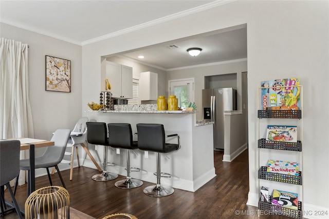 kitchen featuring dark hardwood / wood-style floors, kitchen peninsula, stainless steel fridge, light stone countertops, and white cabinets