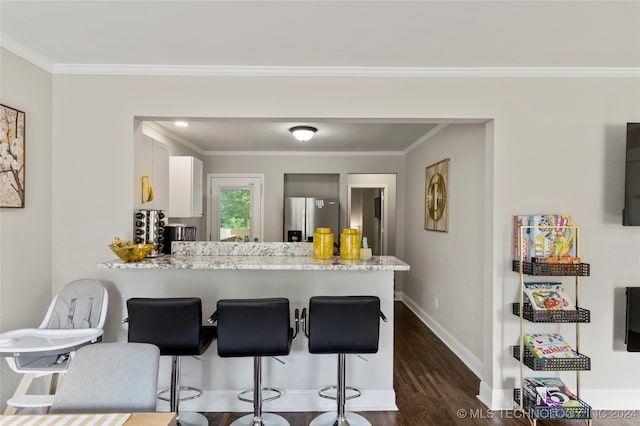 kitchen with dark hardwood / wood-style floors, stainless steel refrigerator with ice dispenser, kitchen peninsula, a kitchen bar, and white cabinetry