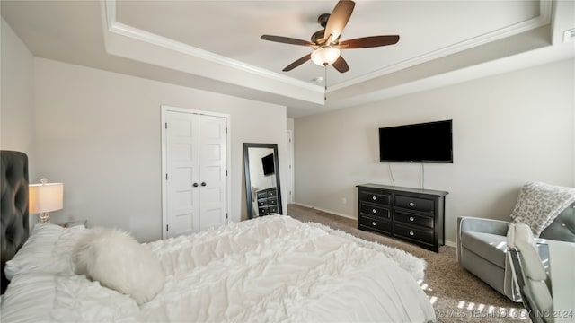 carpeted bedroom with a closet, ceiling fan, a raised ceiling, and ornamental molding