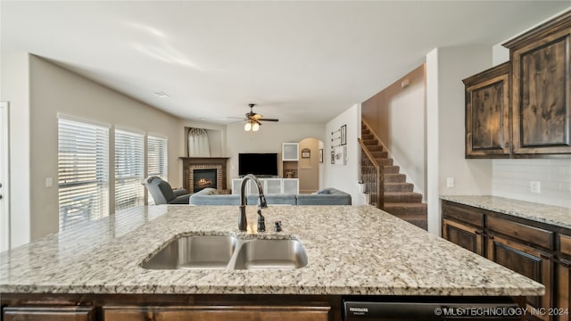 kitchen with decorative backsplash, light stone counters, a fireplace, dark brown cabinetry, and sink