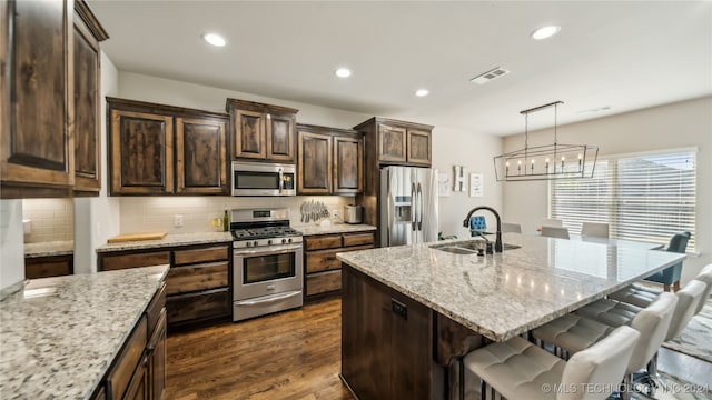 kitchen featuring a center island with sink, light stone countertops, hanging light fixtures, and stainless steel appliances