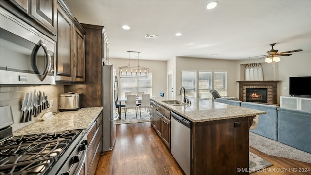 kitchen featuring sink, an island with sink, a brick fireplace, stainless steel appliances, and dark hardwood / wood-style floors