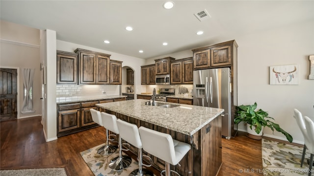 kitchen with appliances with stainless steel finishes, sink, a kitchen island with sink, and dark hardwood / wood-style flooring