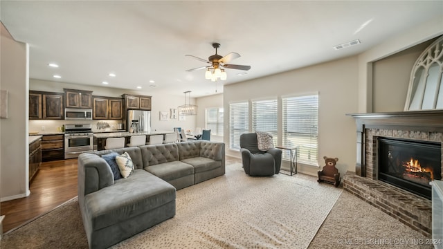 living room featuring ceiling fan, hardwood / wood-style flooring, and a brick fireplace