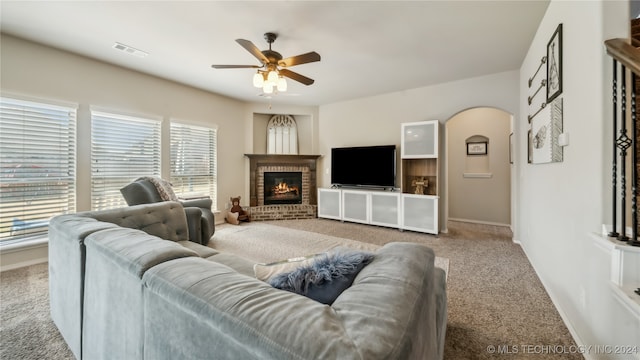 carpeted living room featuring a brick fireplace and ceiling fan