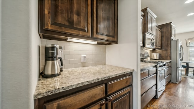 kitchen featuring decorative backsplash, dark hardwood / wood-style floors, dark brown cabinetry, appliances with stainless steel finishes, and light stone counters