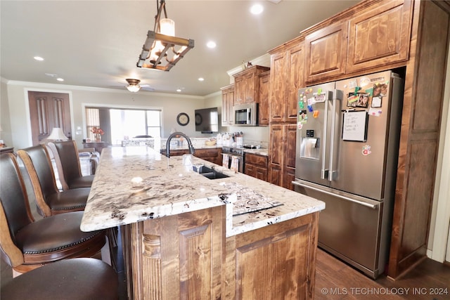 kitchen with stainless steel appliances, a large island with sink, sink, a breakfast bar area, and decorative light fixtures