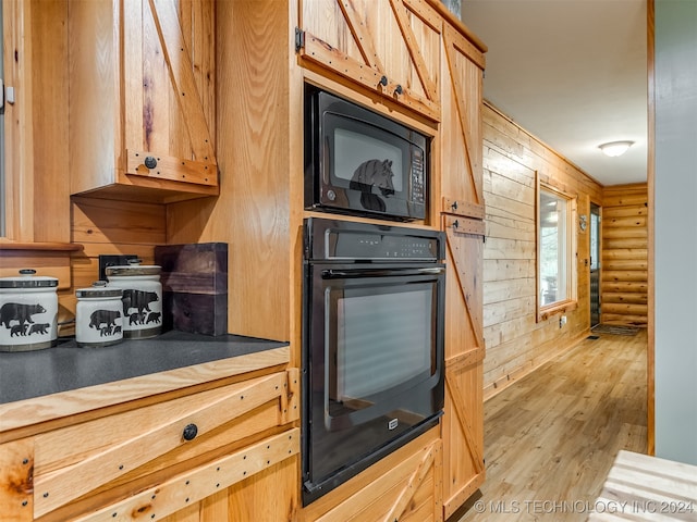 kitchen with light wood-type flooring, light brown cabinetry, wooden walls, and black appliances