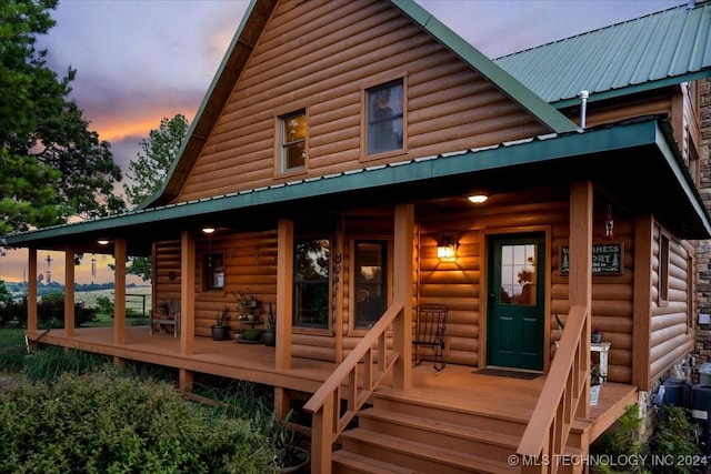 back of property at dusk featuring metal roof, a porch, and log veneer siding