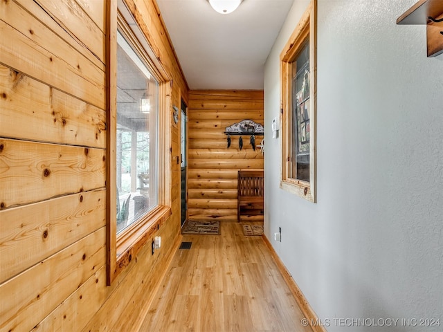 corridor with a textured wall, rustic walls, light wood-style flooring, and baseboards