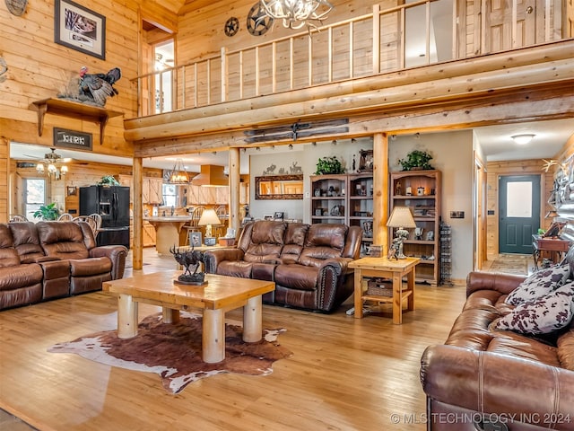 living room with light wood-style flooring, a notable chandelier, wooden walls, and a high ceiling