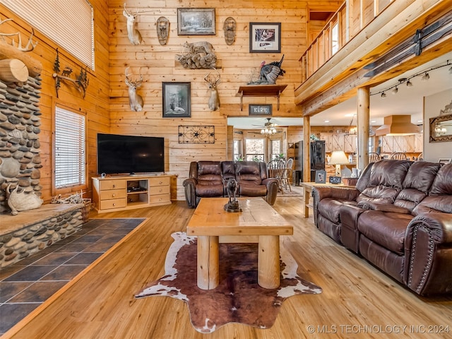 living room with a towering ceiling, light hardwood / wood-style floors, wood walls, and ceiling fan