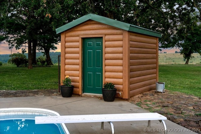 outdoor structure at dusk with a yard, an outdoor pool, an outdoor structure, and a storage shed