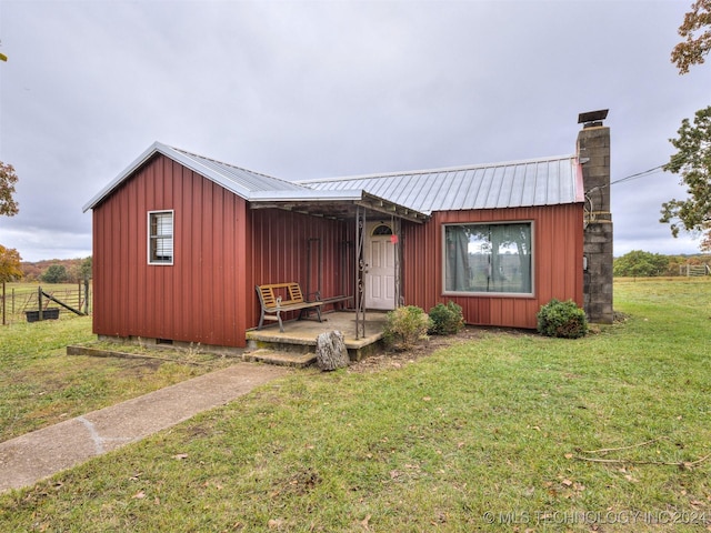 view of front facade with metal roof, crawl space, board and batten siding, a chimney, and a front yard