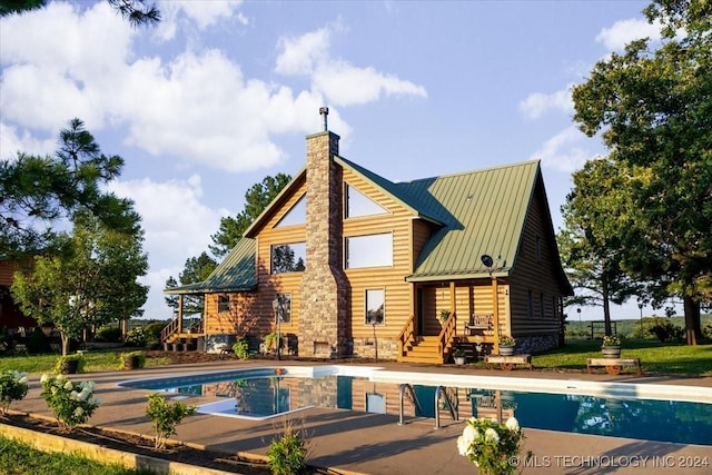 rear view of property featuring an outdoor pool, metal roof, a chimney, and a standing seam roof